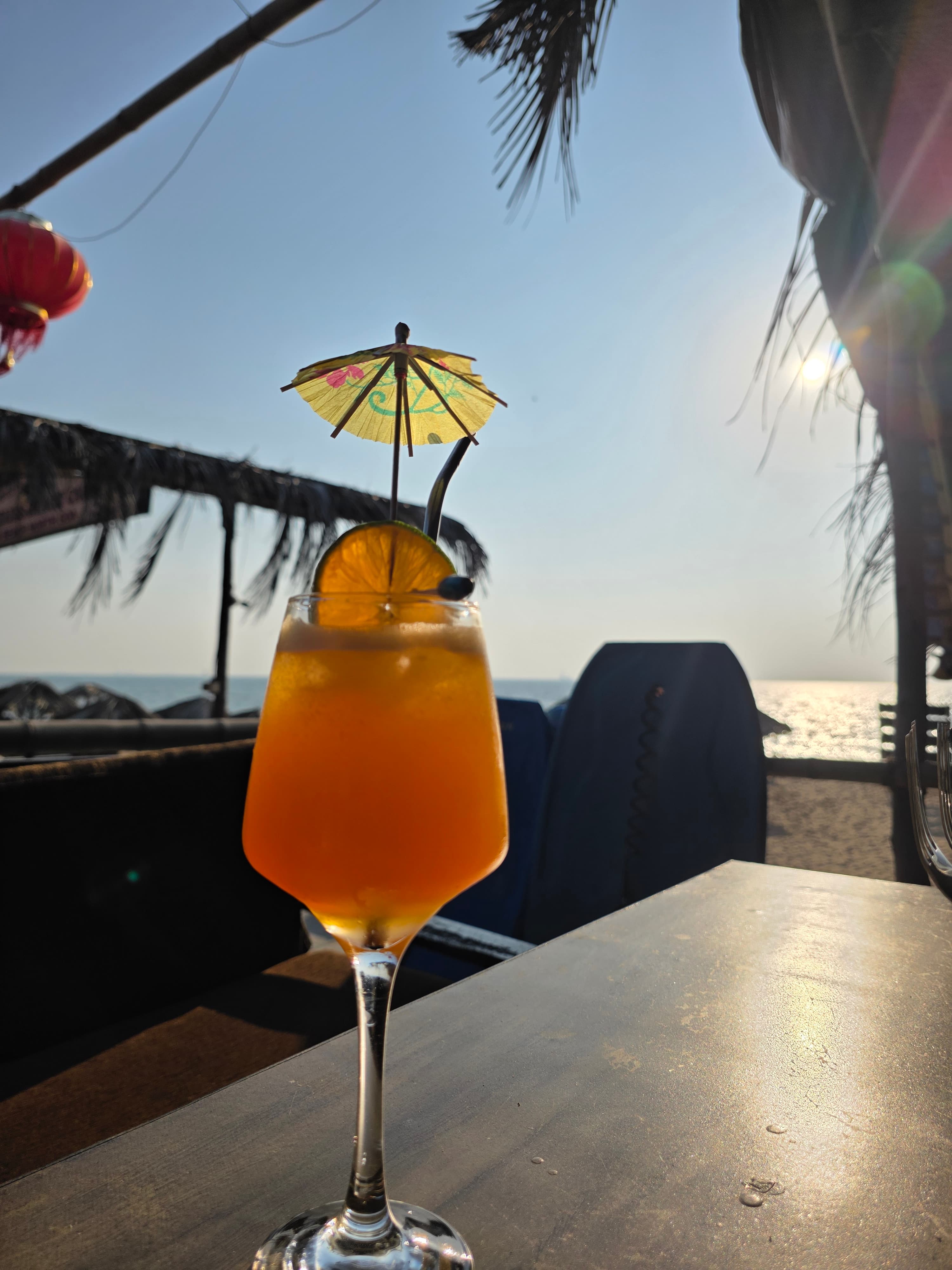 Amber cocktail with paper umbrella and citrus slice in stemmed glass, ocean glimmering at sunset behind
