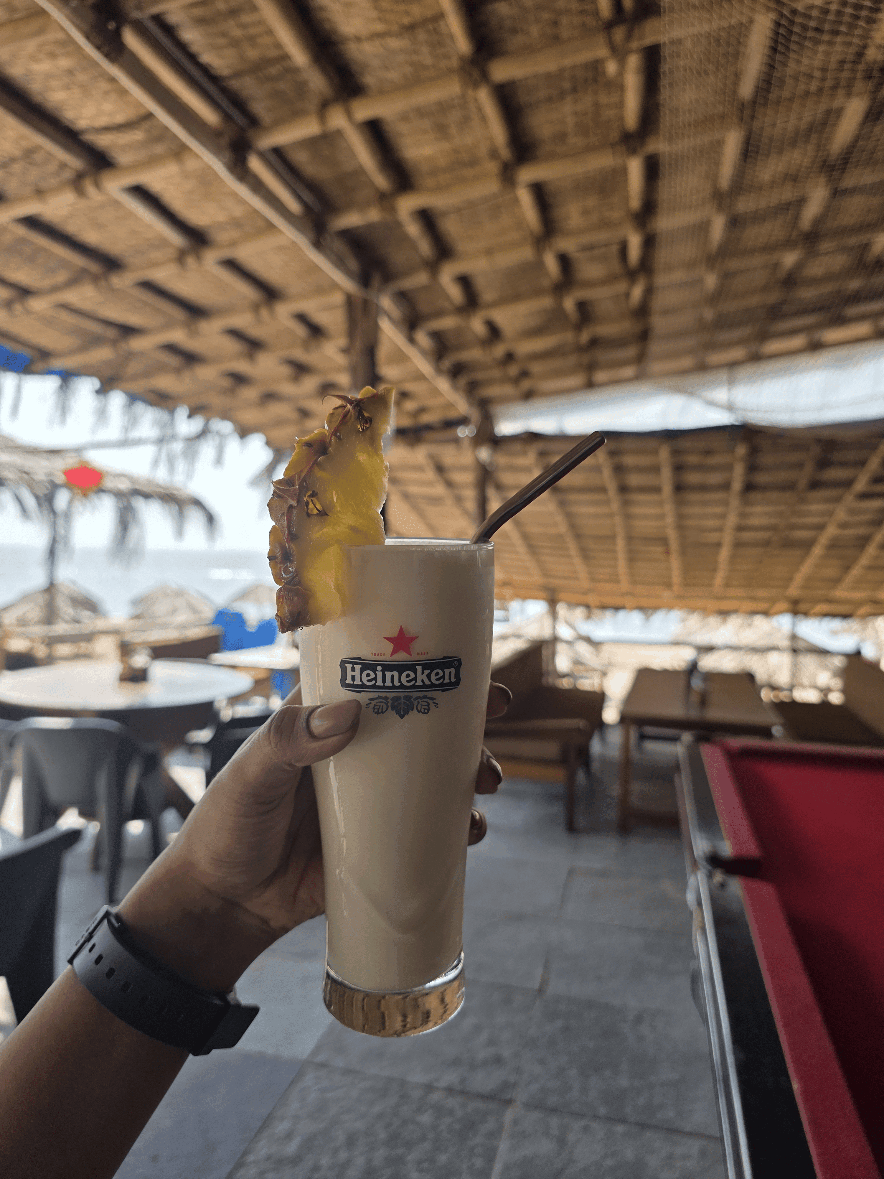 Coconut-cream cocktail topped with pineapple in a tall glass held up inside the beach lounge with sea glimpsed behind