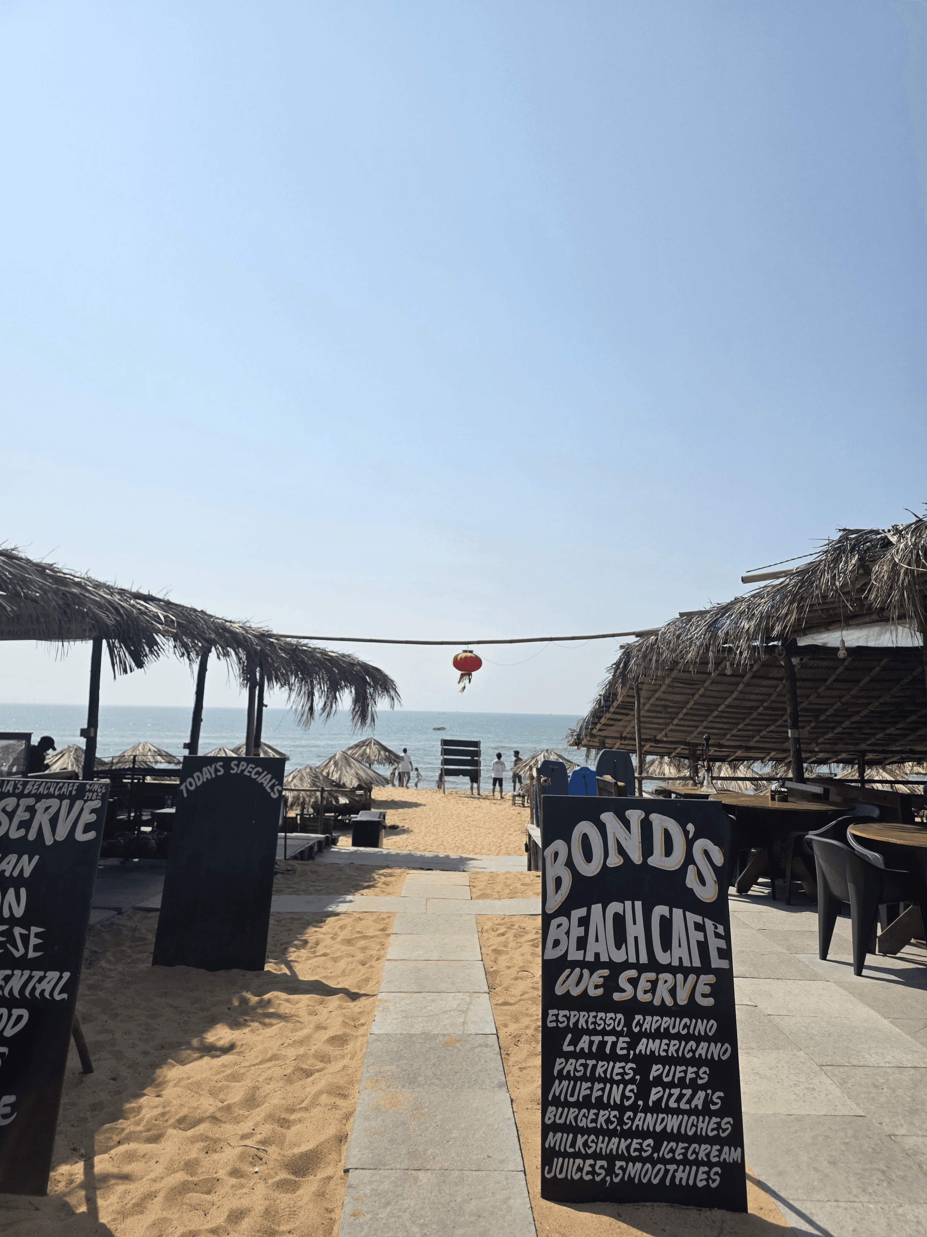 Bond's Beach Cafe entrance with chalkboard menus, thatched seating areas and sandy path leading to the ocean