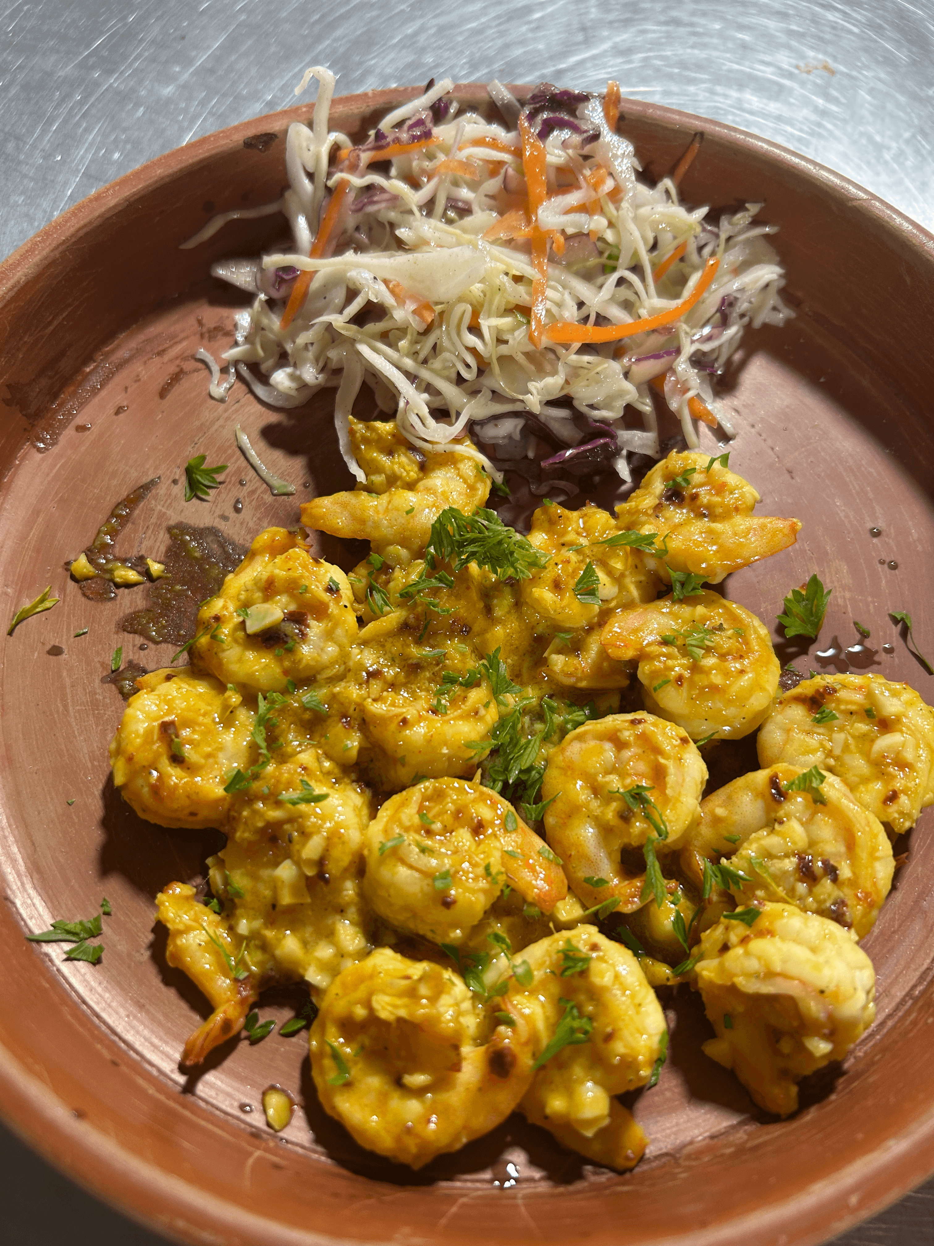Spiced coastal prawns in golden curry sauce with crisp coleslaw salad on a terracotta plate