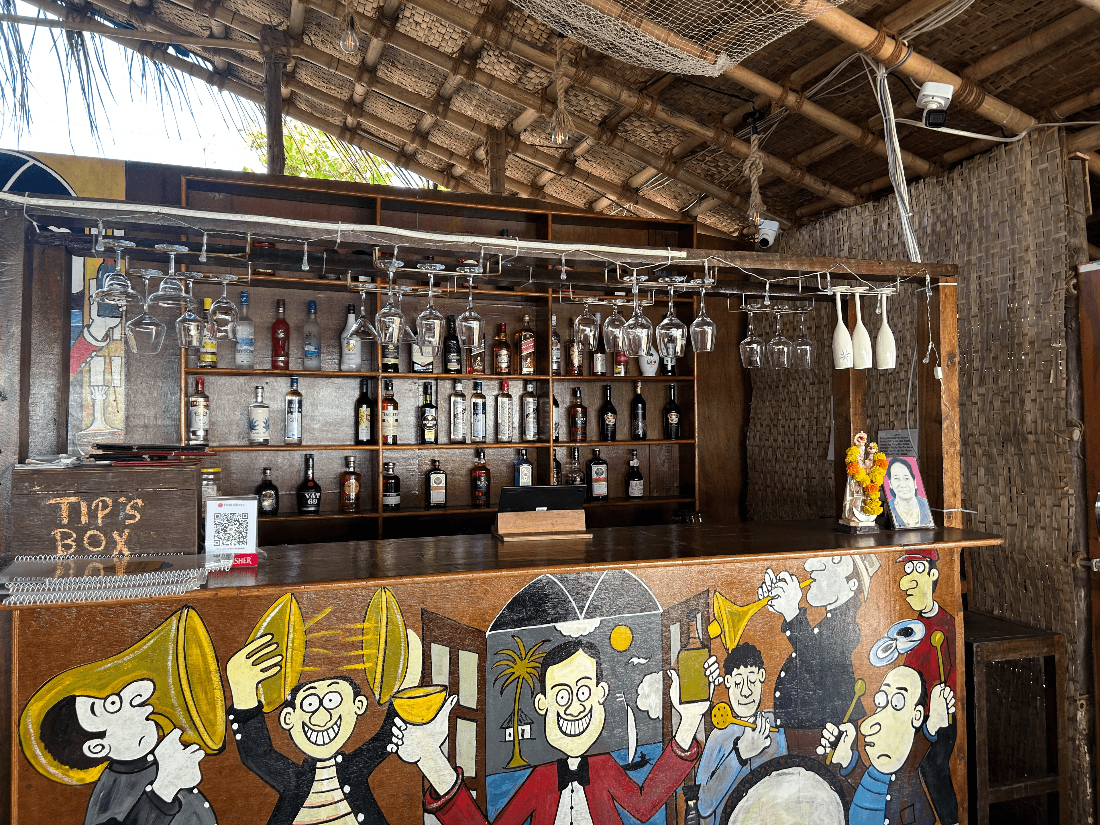 Interior bar view showing glass rack overhead, stacked spirit bottles and painted mural counter at Bonds Beach Cafe